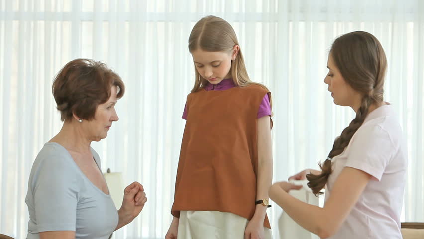 Girl trying on a dress with a top and a silk belt, two women helping her