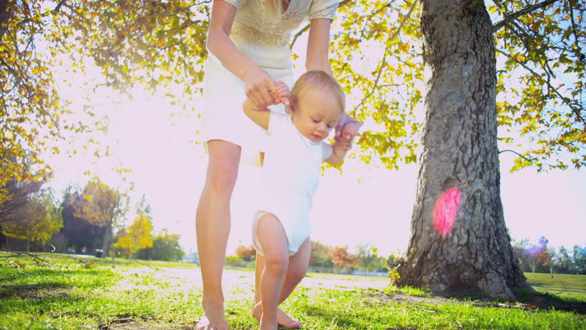 Caucasian mother supporting her little baby as he practices his first steps
