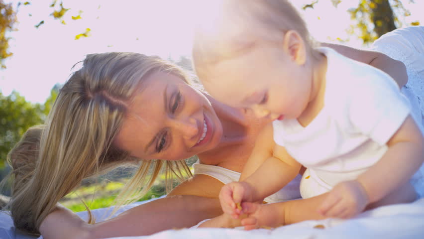Caucasian mother lying outdoors on the grass and tenderly kissing her cute baby