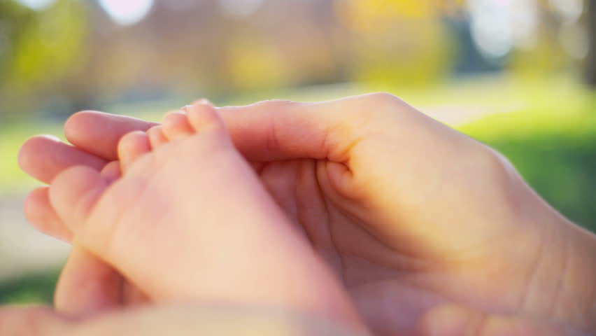 A mothers hands in close up cradling the foot of her baby