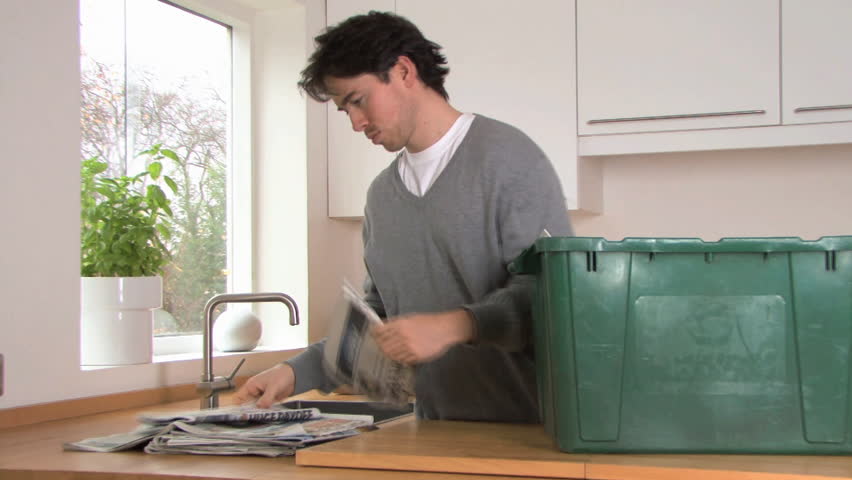 MEDIUM SHOT PAN OF A MAN RECYCLING NEWSPAPER