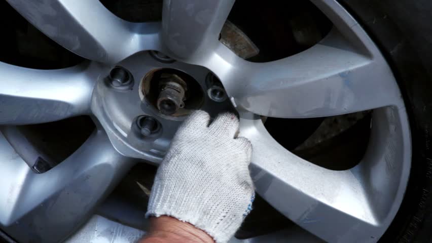 Hands in glove screw up nuts on car wheel, closeup view