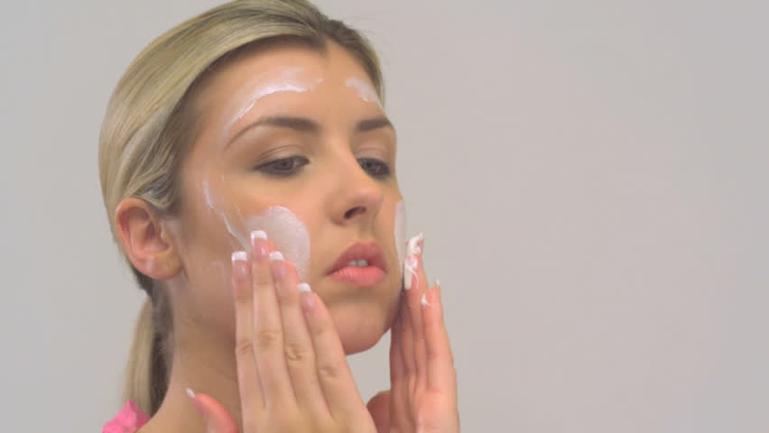 CLOSE UP OF A YOUNG WOMAN MOISTURIZING HER FACE ON WHITE BACKGROUND
