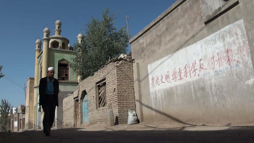 HOTAN - 10 SEPTEMBER 2010: People walk past mosque and Communist text. Hotan has historically been a convenient meeting place on Silk Road where goods, technologies, philosophies and religions are exchanged between cultures.