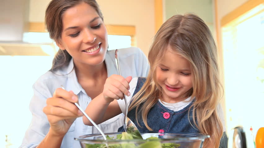 Little girl mixing salad with her mother in the kitchen