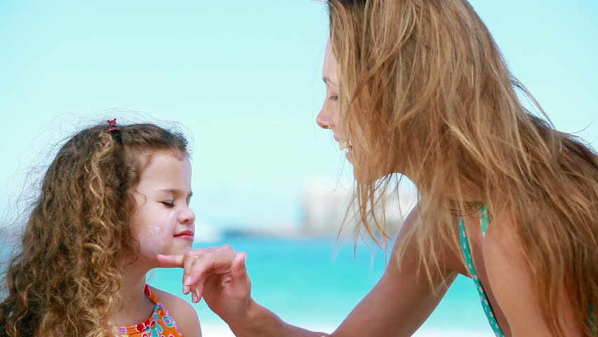 Mother applying sunscreen on a little girl on the beach