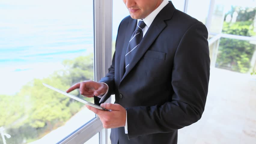 Man in suit using a tablet computer while standing in a building beside the sea