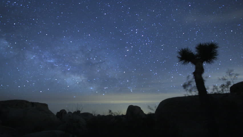 Majestic long-exposure time lapse shot of the Milky Way and Stars Galaxy. Passing over Joshua Tree Desert. Fades up to an overexposed white as the sun rises.