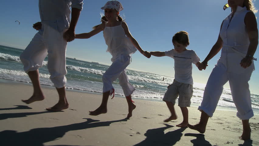 MEDIUM CLOSE UP LOW ANGLE VIEW PAN OF GRANDPARENTS RUNNING ALONG A BEACH WITH THEIR GRANDCHILDREN