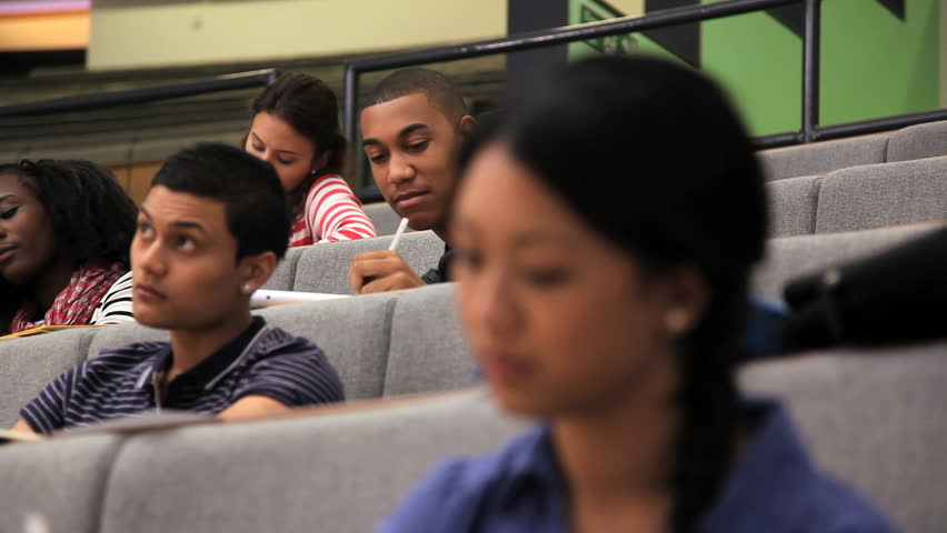 CLOSE UP of female and students taking notes in lecture theatre