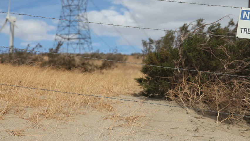 panning left to right tumble weed blowing in the wind with no trespassing sign and barbed wire in background