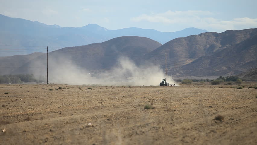Tractor plowing up desert brush with dust blowing around