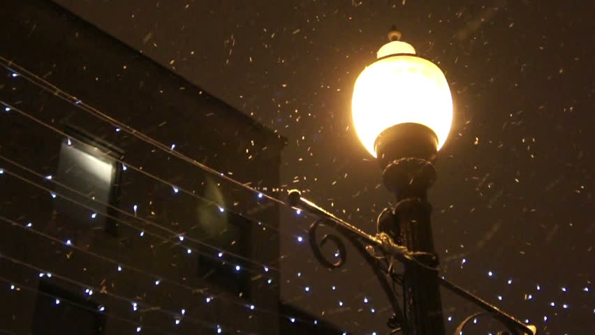 Snow falling by night near a street lamp.