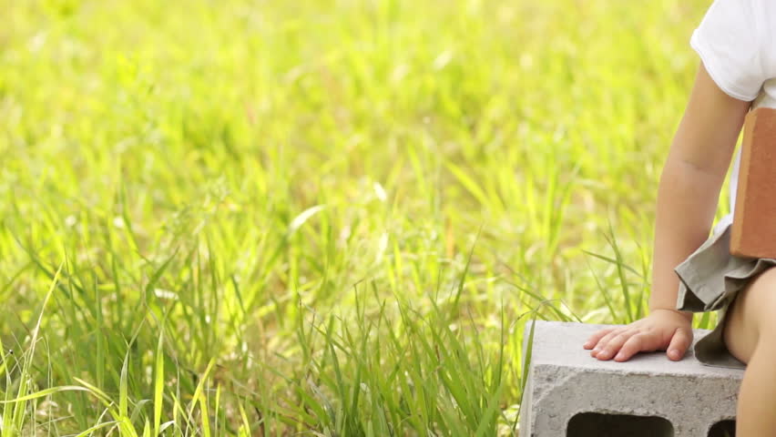 Girl in hard hat sitting on cinder block gives thumbs up