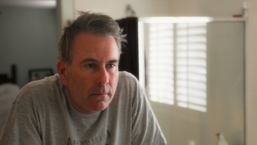 camera zooming on man looking into bathroom mirror with introspective stare