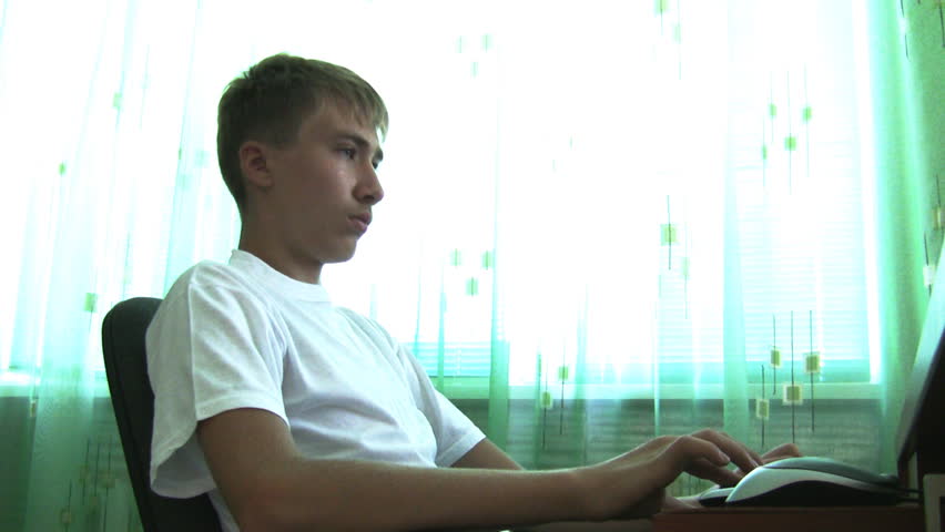 teenager attentively looks at monitor of computer and works on  keyboard