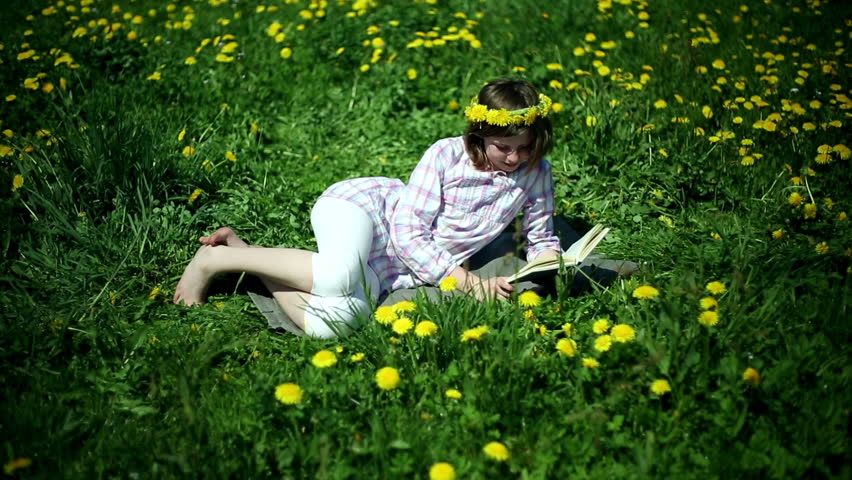 Teenager girl lying on meadow full of sow-thistle and reading book