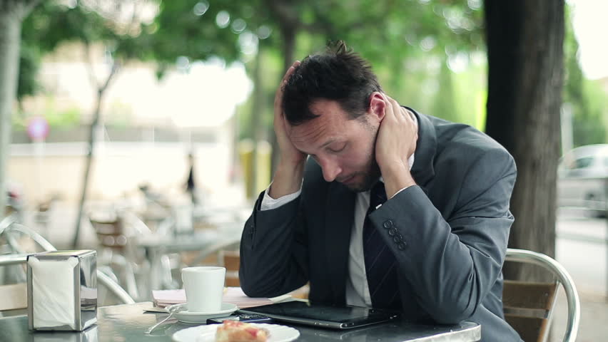 Young businessman reading bad news on tablet computer in cafe
