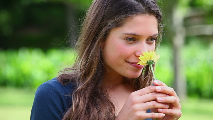 Smiling young woman smelling a flower in a park