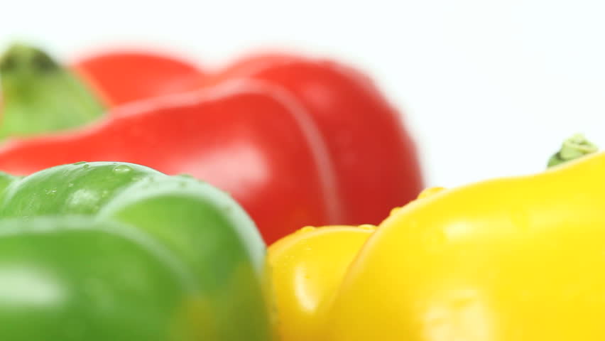 Three tasty big peppers in vivid colors slowly spinning in a seamless loop, red yellow and green paprika tops close-up on white background