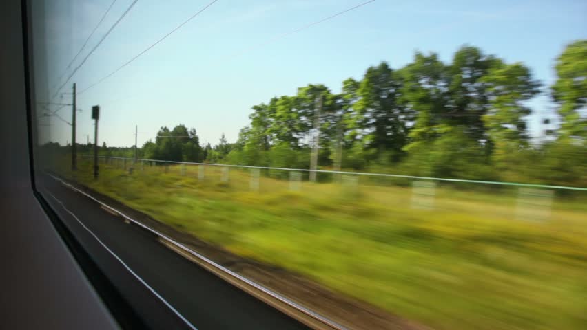 Plants and pillars with wires pass by during train trip at summer day