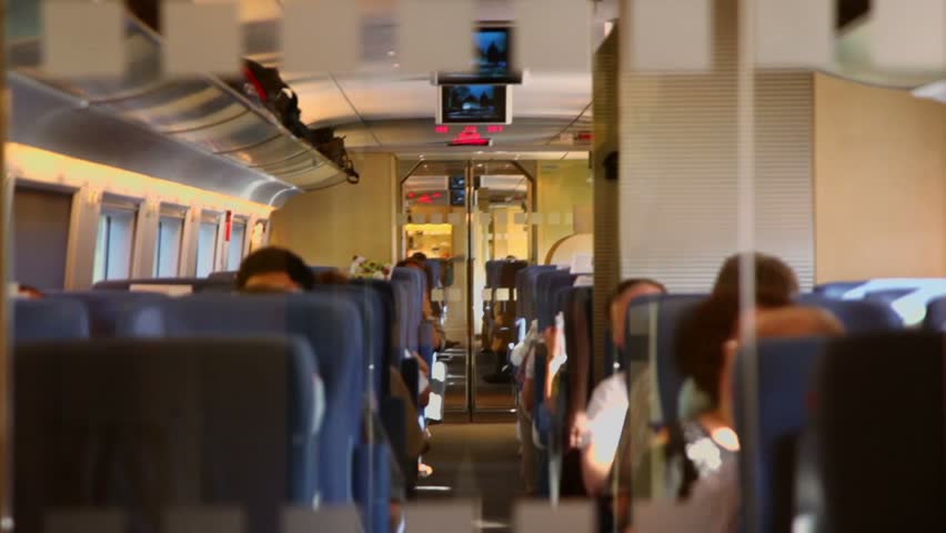 People sit inside coach with digital screen under ceiling