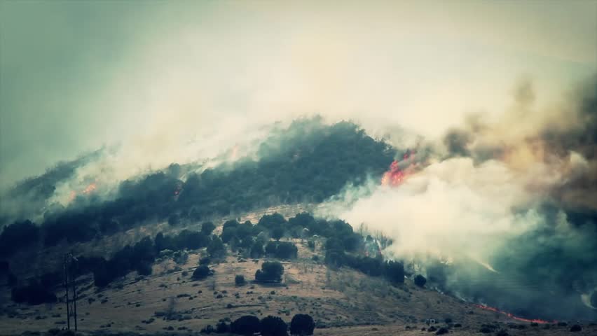 A raging wildfire burns across the mountain leaving a trail of smoke and ash.