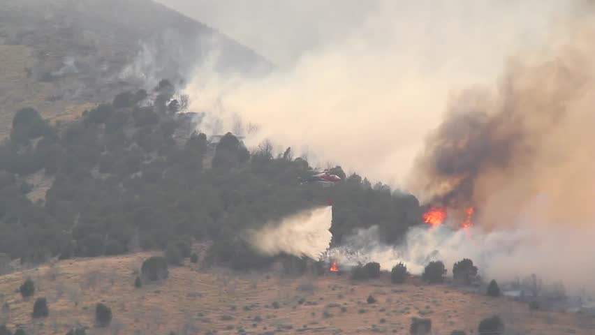 A helicopter battles a gigantic wildfire on a dry mountainside, dropping hundreds of gallons of water on the flames.