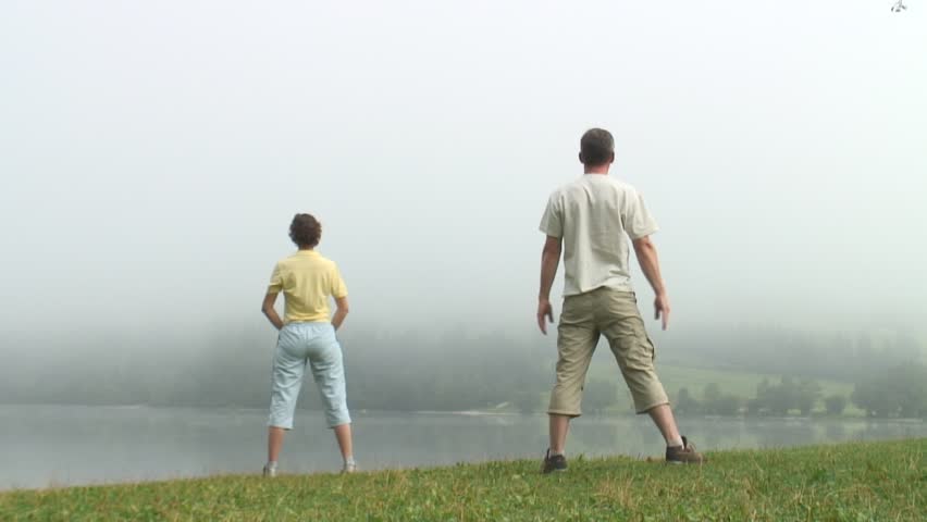 Couple doing gymnastics early in the morning at a lake in the mist.