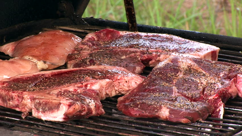 Steaks and chicken being arranged on a barbecue grill, then the lid closes. 