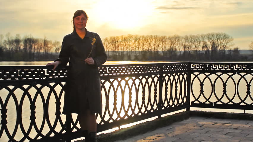 pretty lady with flower that lean on railings near clear lake, sunset