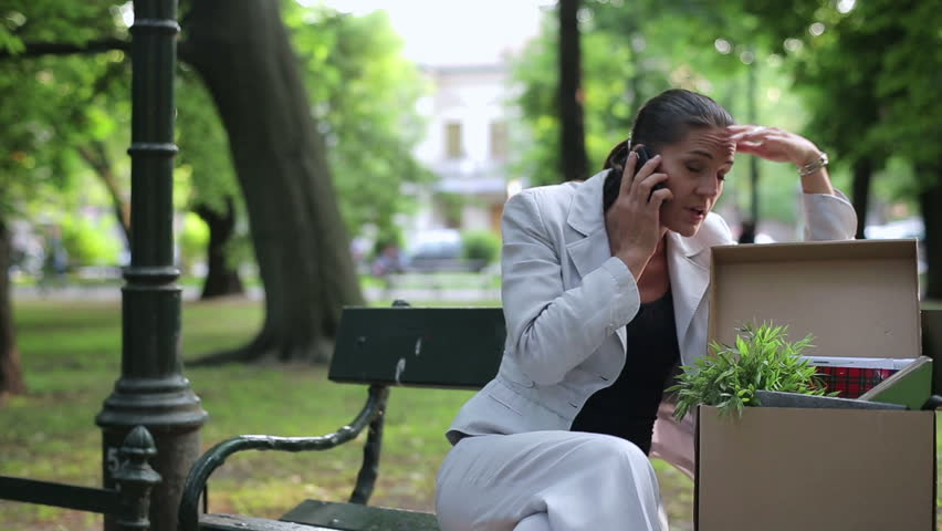 Just fired, unemployed sad young businesswoman talking on cellphone in the park
