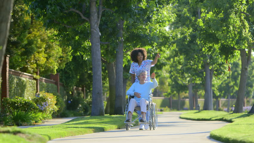 Nurse walking with elderly woman in wheelchair