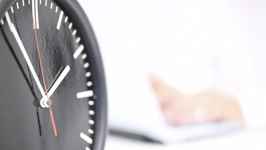 Close up of running clock with business man working on laptop in the back - working time or deadline concept