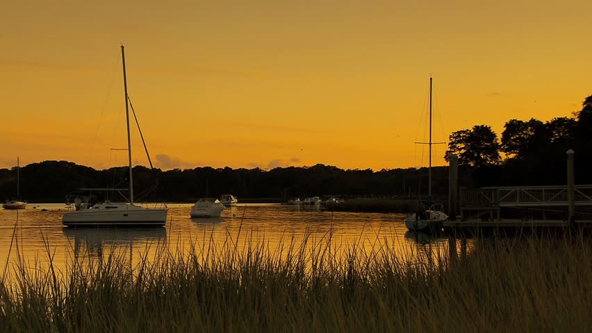 Small cove with sailboats coming towards pier with dramatic orange sunset