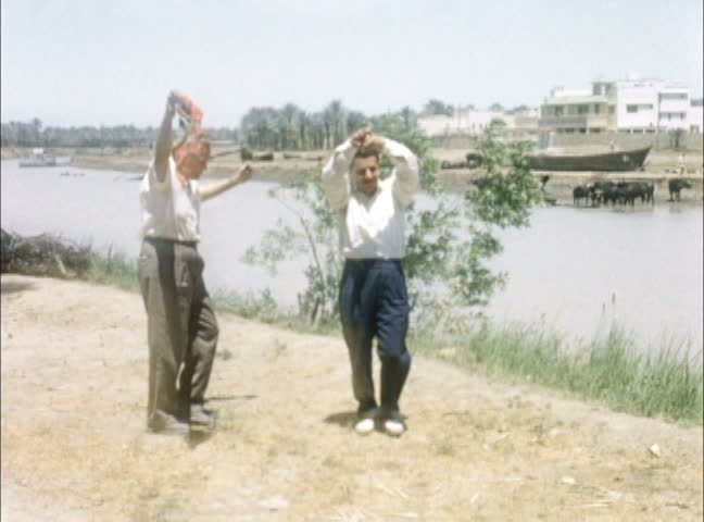 IRAQ - JULY 1956: American tourist dances with Iraqi guide along banks of the Euphrates, Iraq. Shot on 16mm film.