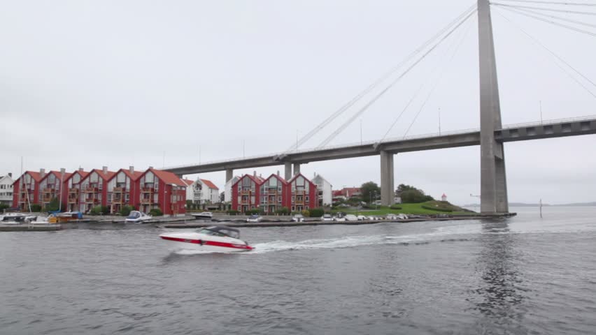 Motorboat and cruiser float near coast with houses under huge pendant bridge
