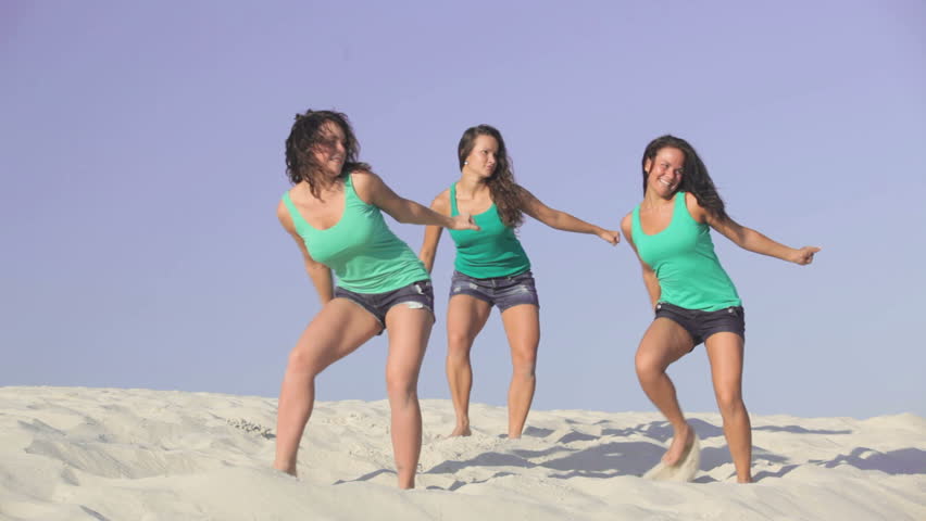 Team of pretty energetic girls dancing on the sand together