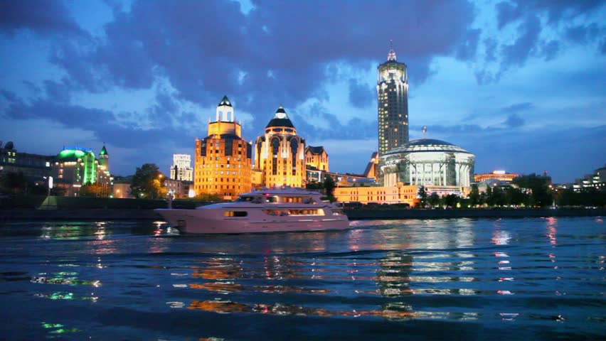 Two ships float down the river near house of music located on quay at night in Moscow