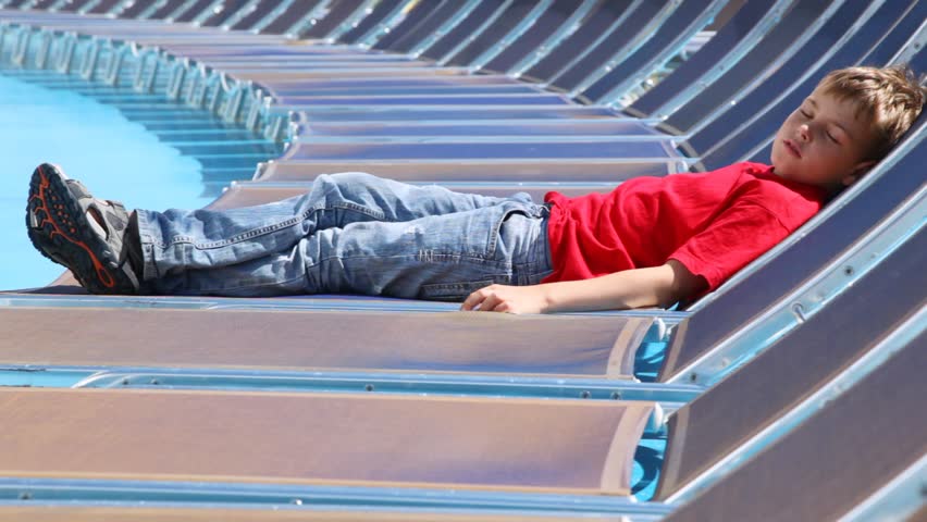 Boy sleeps in chaise lounge on ship deck in sunny weather in afternoon