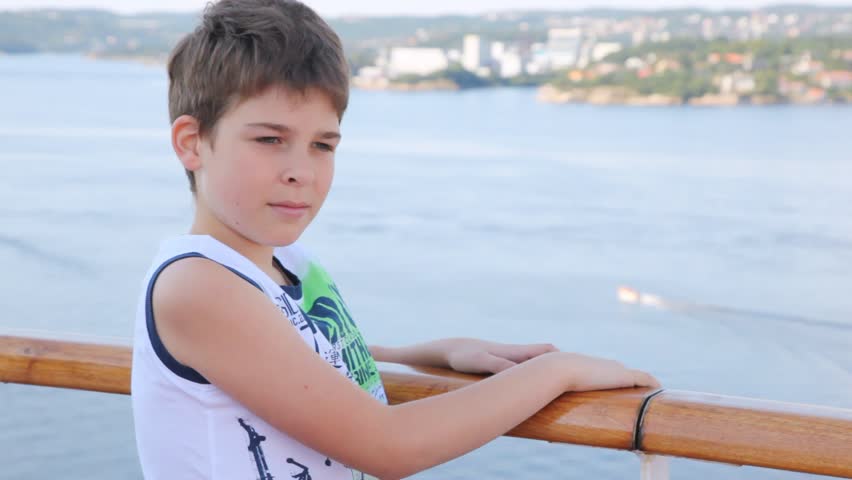 Boy stands on ship deck against sea and city in afternoon