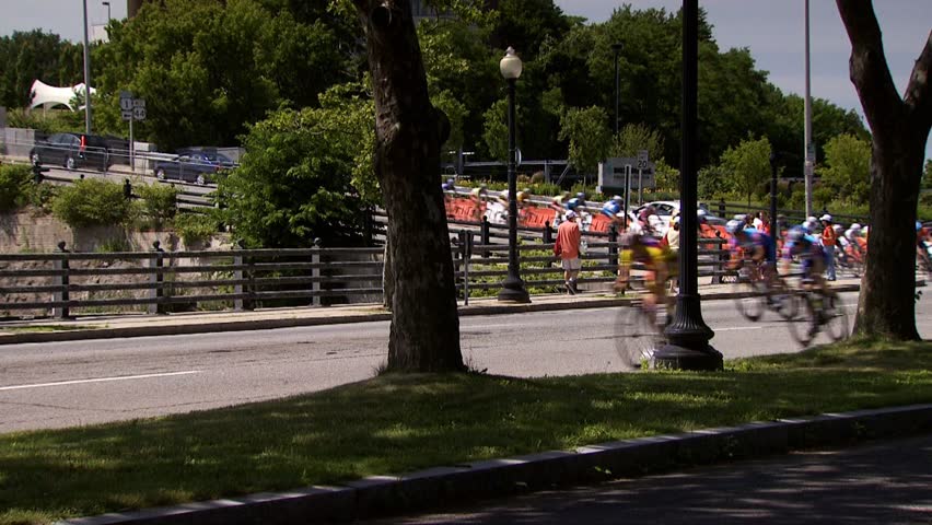 PROVIDENCE, RHODE ISLAND - SEPTEMBER 3, 2009: Bicycle racers on city street passing in front of nice trees and grass - slow motion