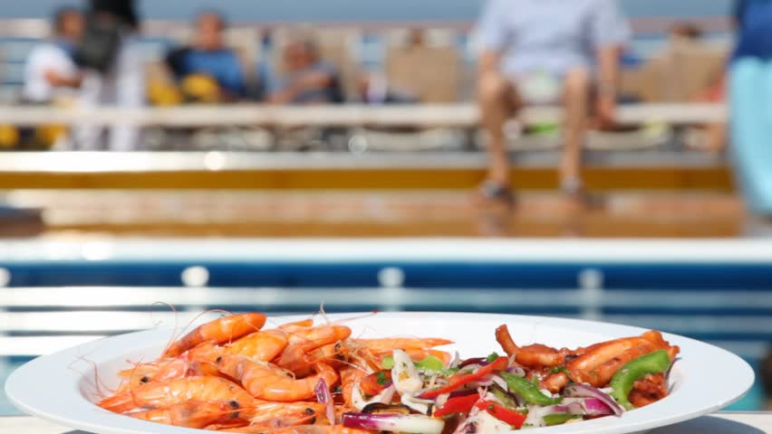 dish with shrimps and salad on table in front of pool and chaise lounges with people close up