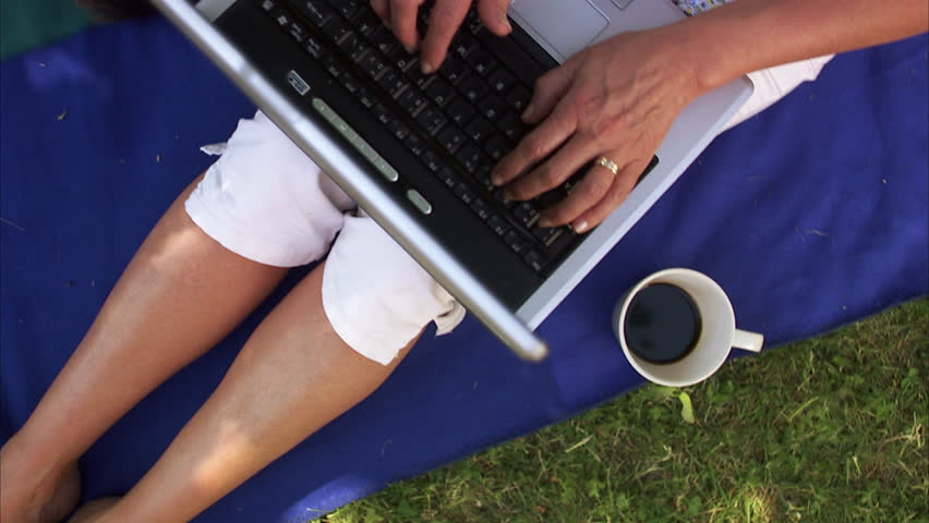 A couple in a park, woman using her laptop and man resting