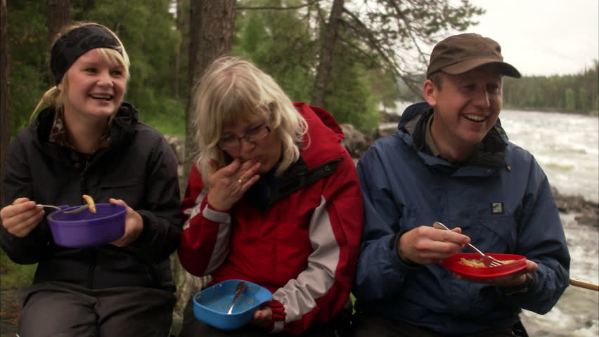 People eating sitting around a camp fire