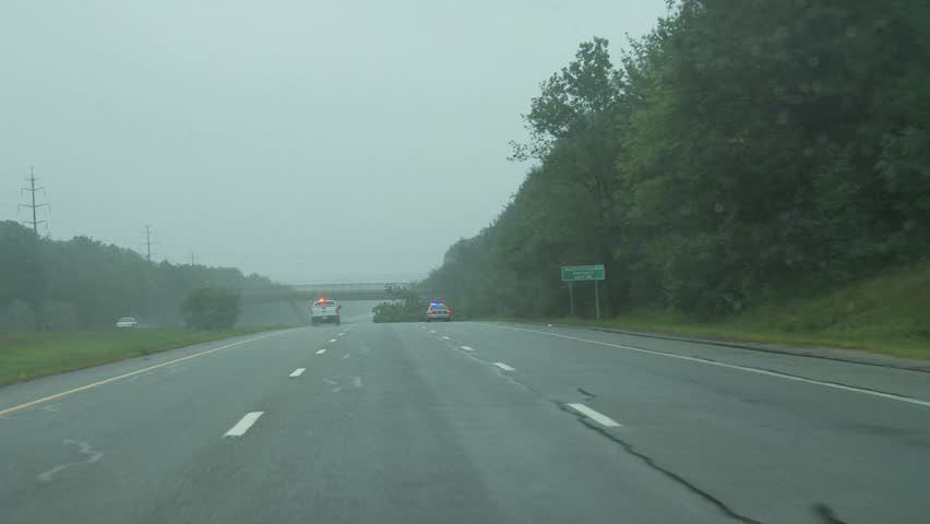 NEW ENGLAND - CIRCA SEPTEMBER 2011: Storm damage -- POV through car windshield as it passes police cars and storm damage on interstate highway