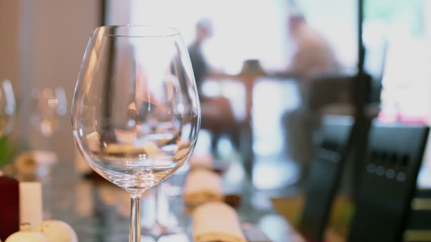 Waiter comes to clients behind waterwall in eastern restaurant with glasses and chopsticks at table, focus changes