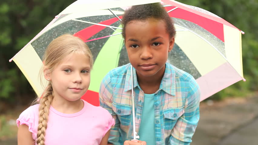 Charming girls hanging out outside in the rain hiding under one umbrella