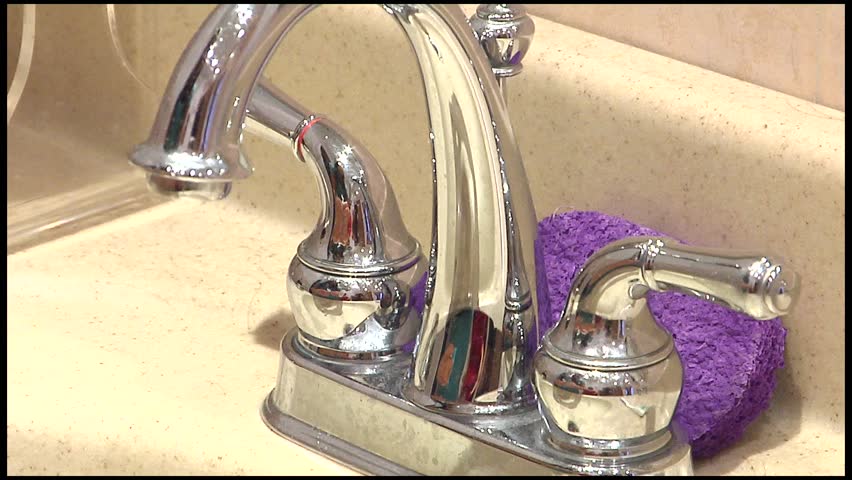 Extreme close up of silver facuet that gets turned on by hand, water runs