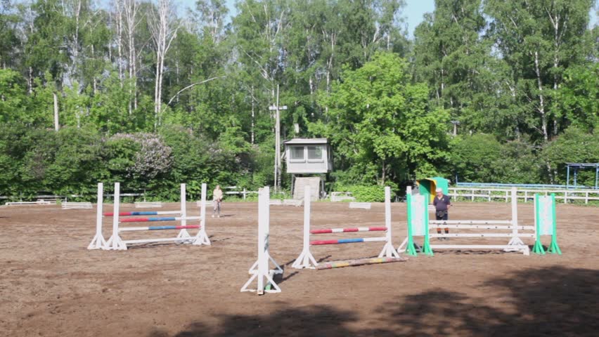 Jockey rides on horseback and jump other bars at equestrian field at sunny summer day